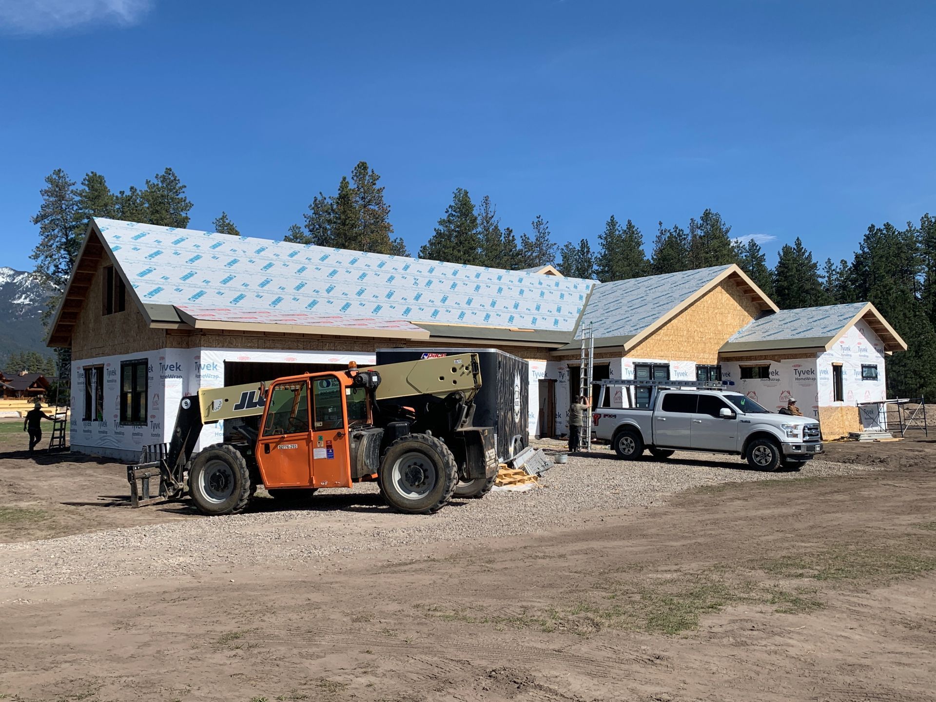 Orange tractor and white pickup parked beside a rural house under construction on a dirt lot.