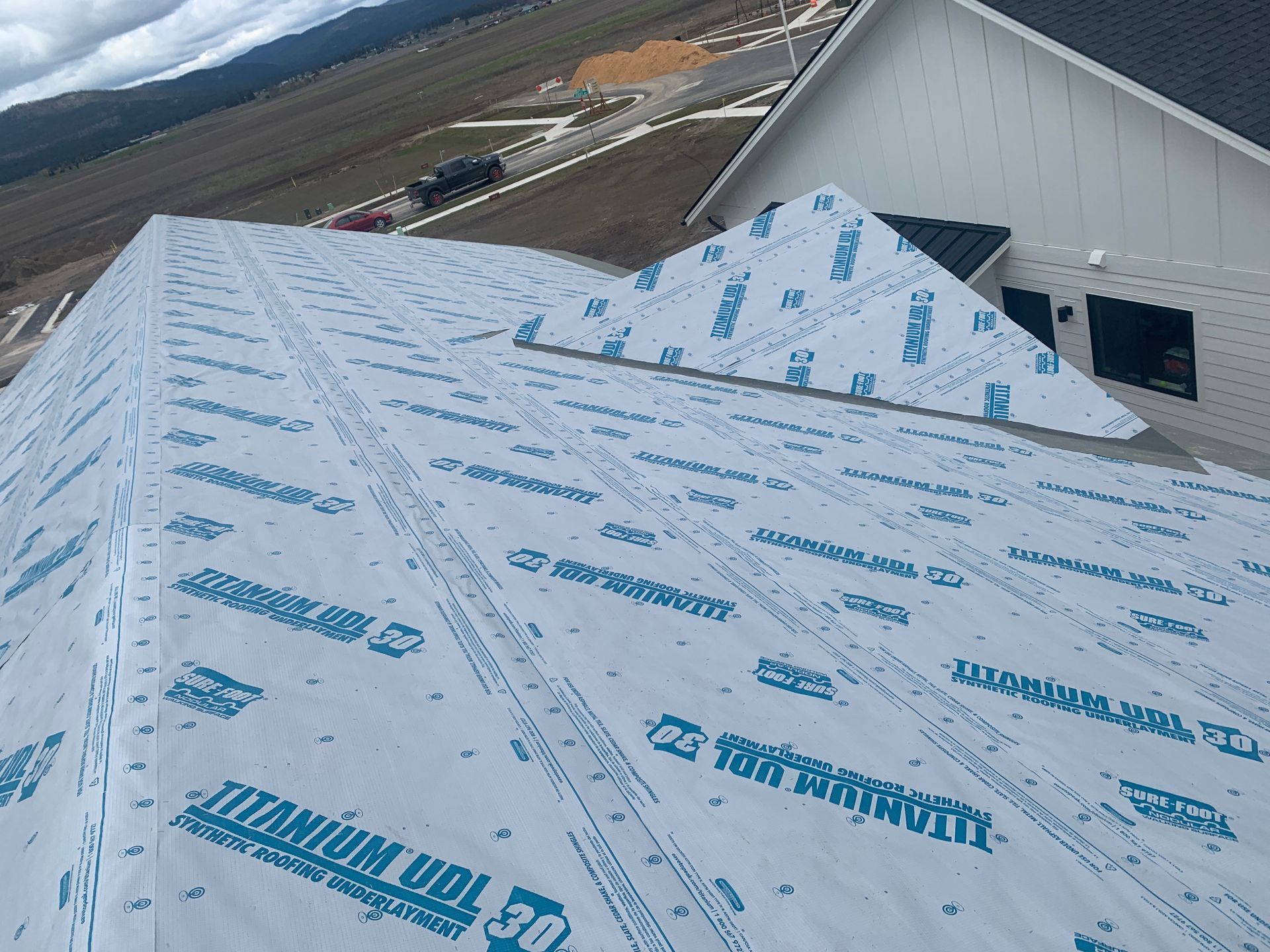 Roof under construction with white waterproof underlayment and a snow-covered mountain in the background