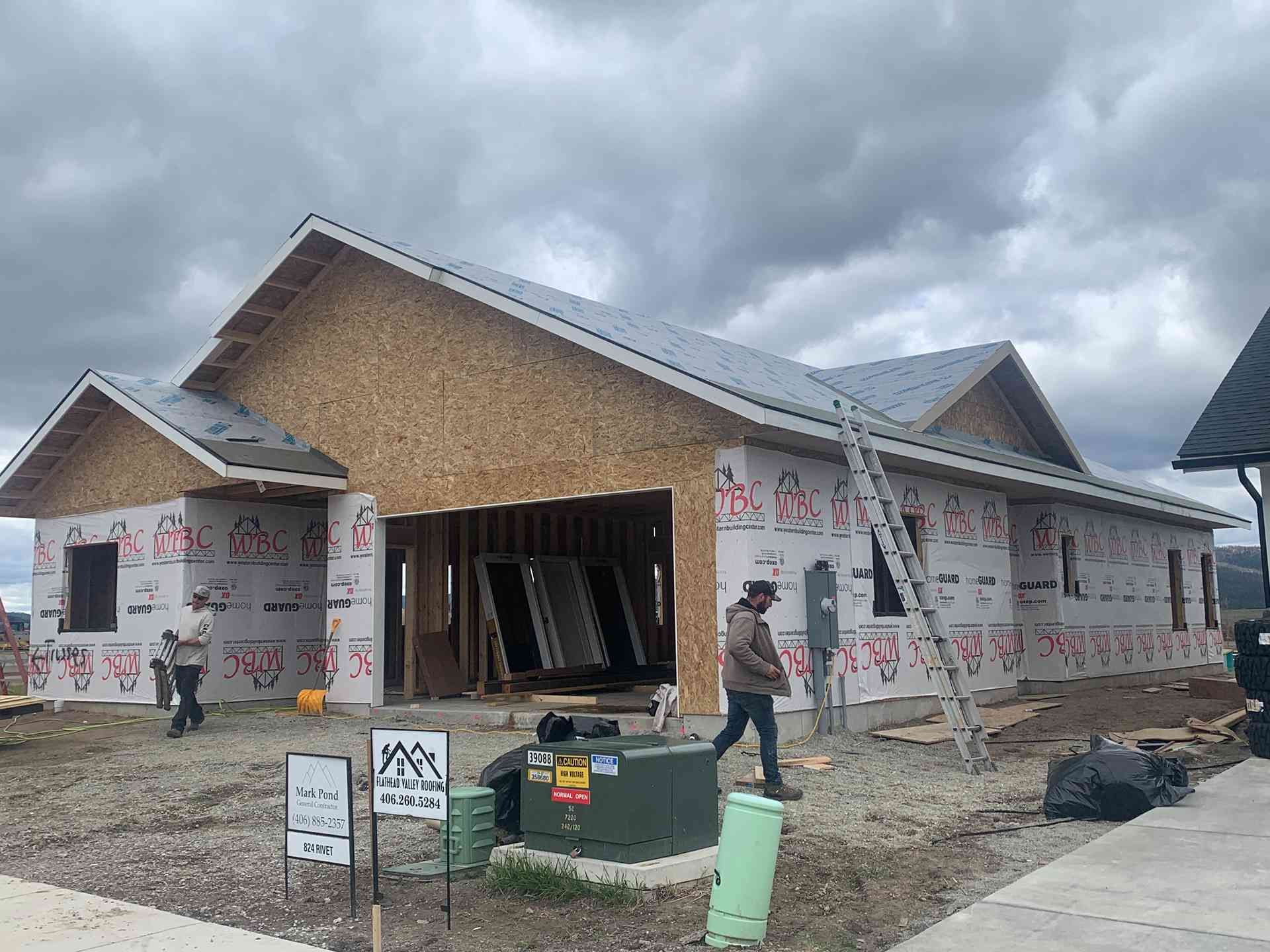 Partially built house with workers, exposed siding, and cloudy sky
