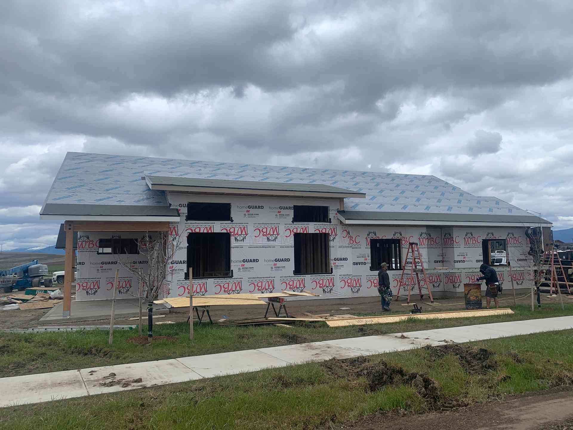 Partially built house with gray roof and wrapped walls under a cloudy sky
