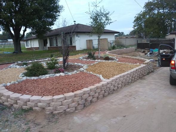 Front yard xeriscape with stone borders, red gravel, small shrubs, and a house in the background