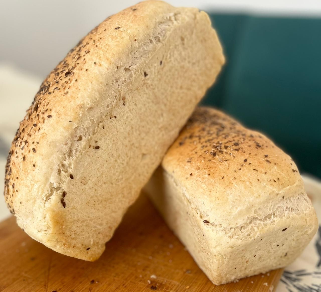 Sobre una tabla de madera descansan dos hogazas de pan de color claro cubiertas con semillas.
