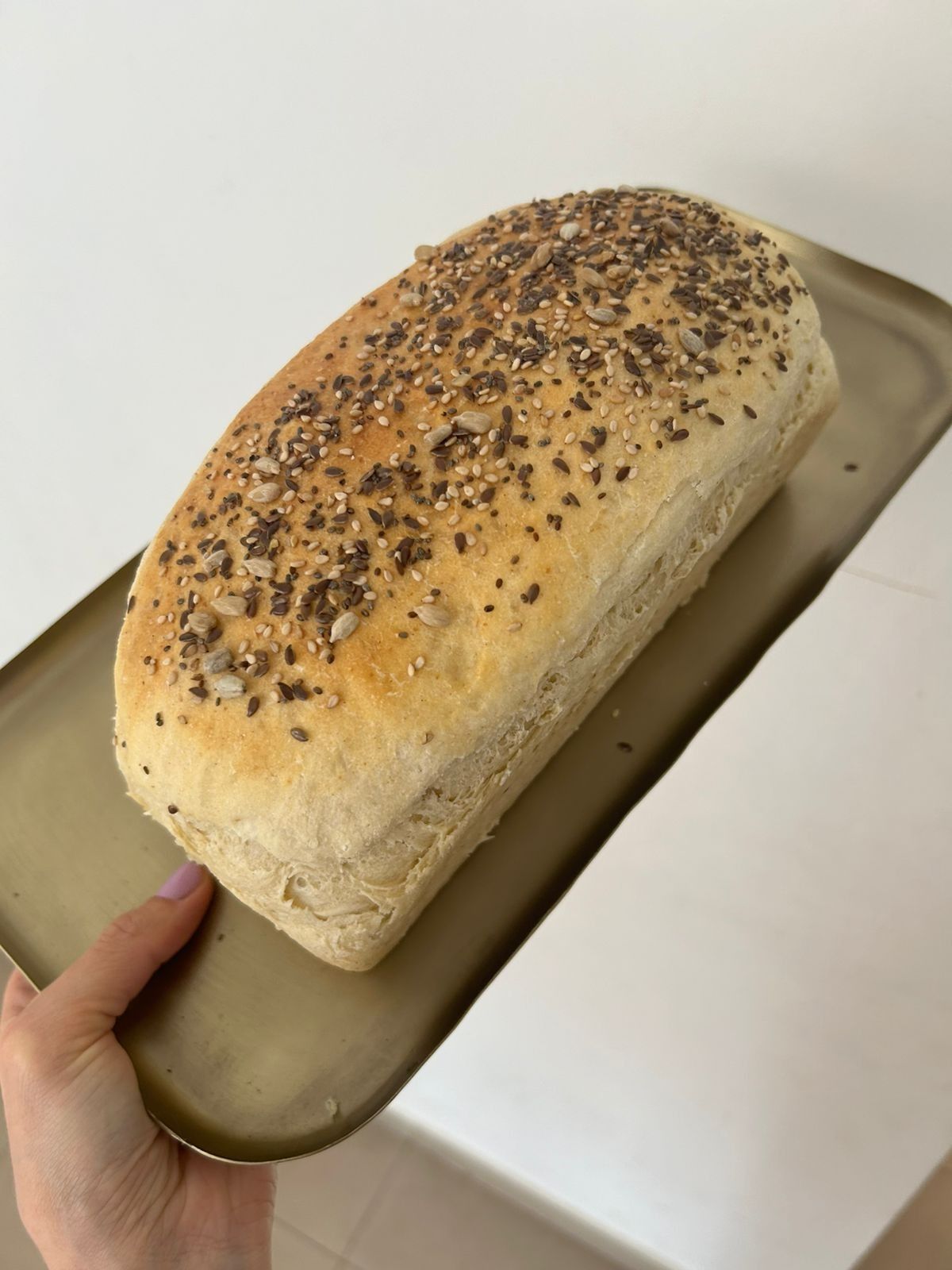 Hogaza de pan con semillas en una bandeja de oro sostenida por una mano.