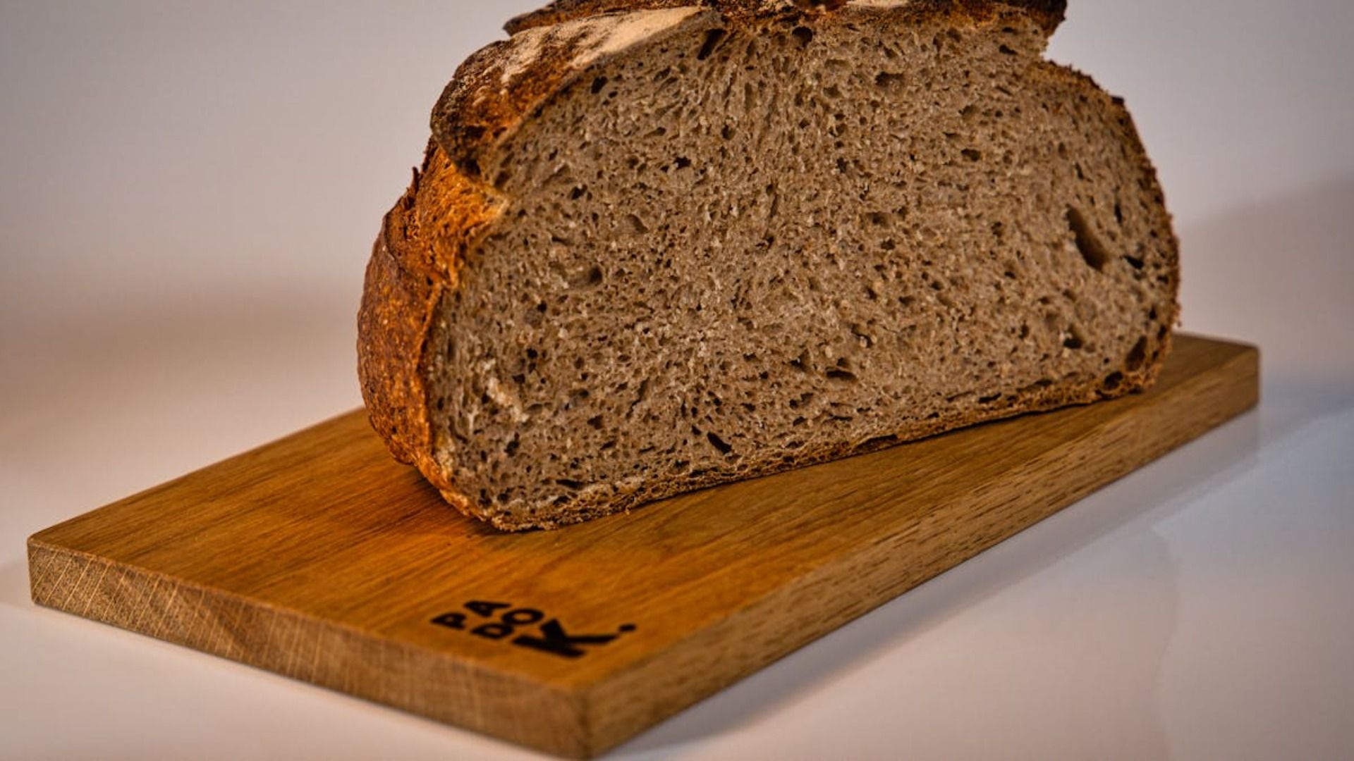 Pan integral cortado en rodajas sobre una tabla de cortar de madera con un logotipo.