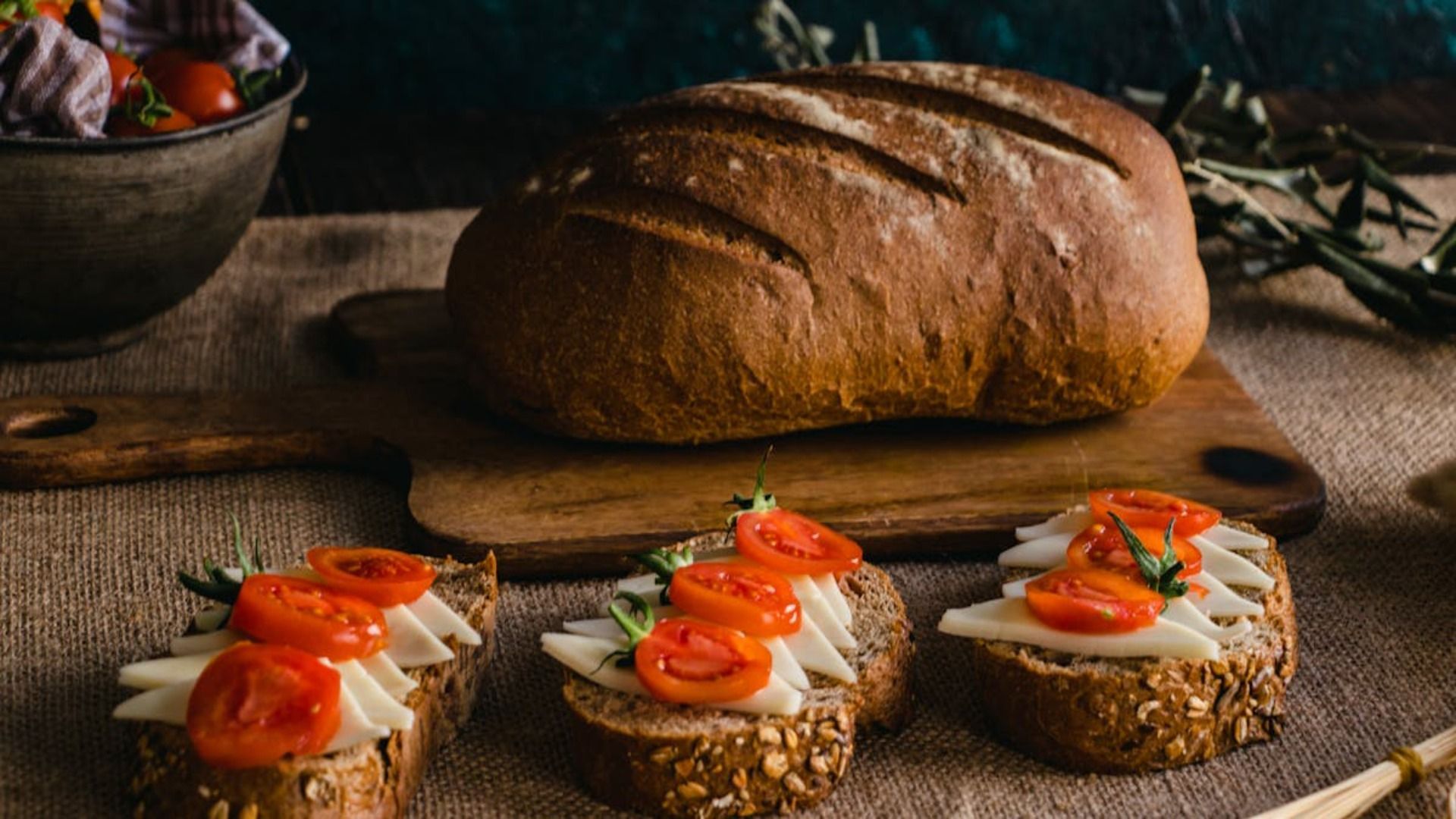 Hogaza de pan con aperitivos de tomate y queso sobre una mesa de madera rústica.