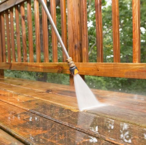 A person is using a high pressure washer to clean a wooden deck.
