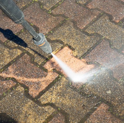 A person is using a high pressure washer to clean a brick sidewalk.