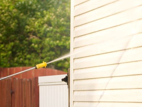 A person is using a pressure washer to clean the side of a house.