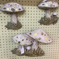 Three decorative mushroom figurines with pale spotted caps and mossy bases on a pegboard display