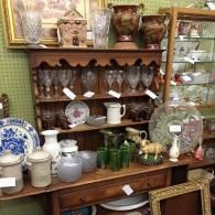 Antique shop display with wooden shelves, glassware, china, pitchers, and decorative dishes.