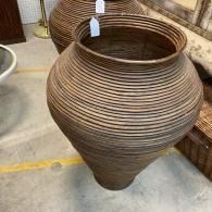 Large brown ribbed ceramic vase on a concrete floor, with woven baskets in the background
