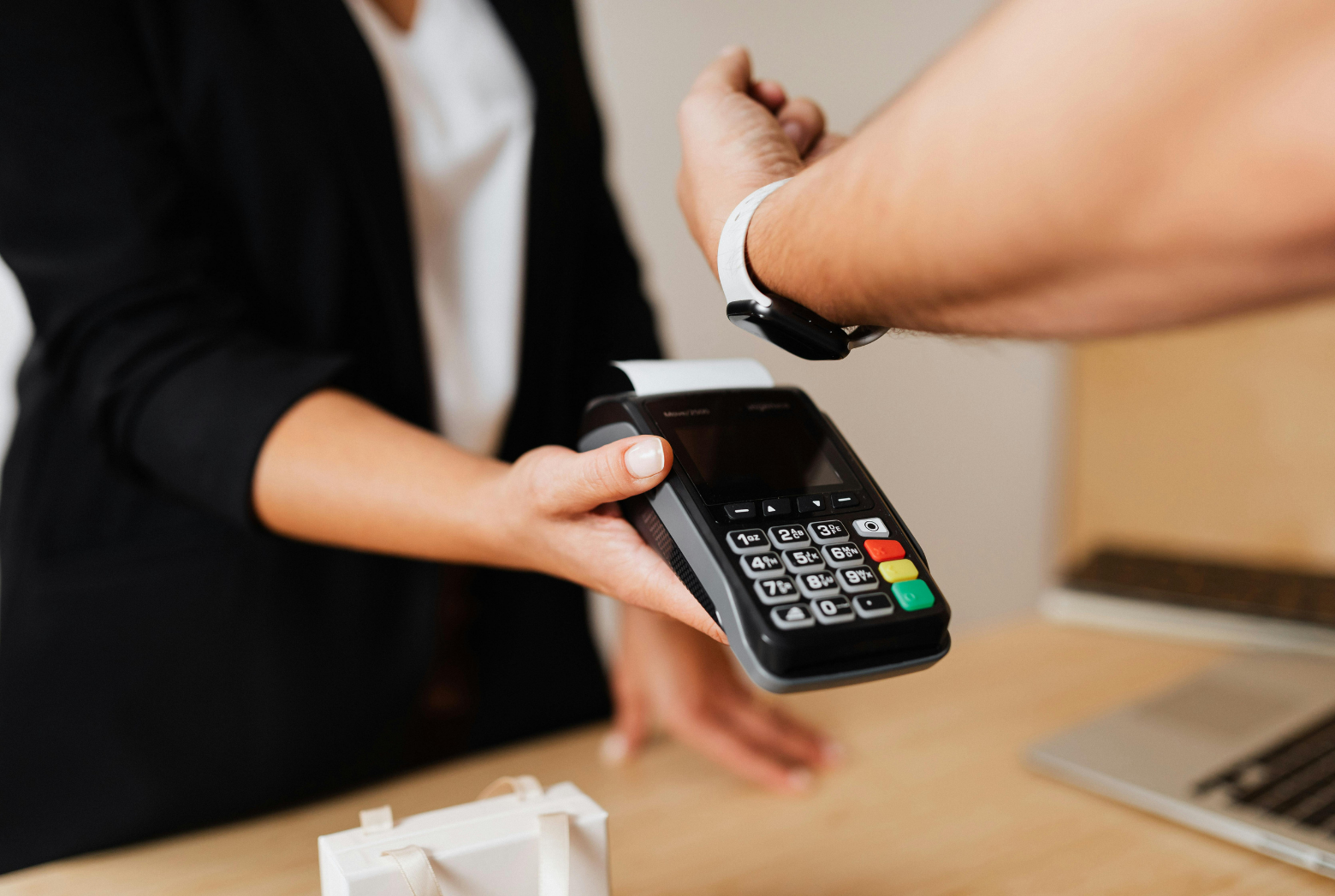 A person pays for a purchase using a smartwatch held over a handheld payment terminal held by another person.