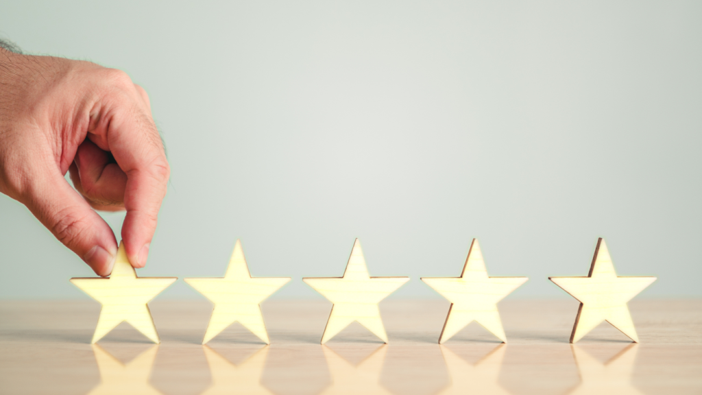 A hand placing the first of five gold-colored star icons in a row on a wooden surface against a neutral background.