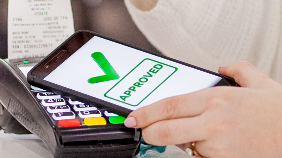 A hand holds a smartphone over a card reader, displaying a green checkmark and the word 