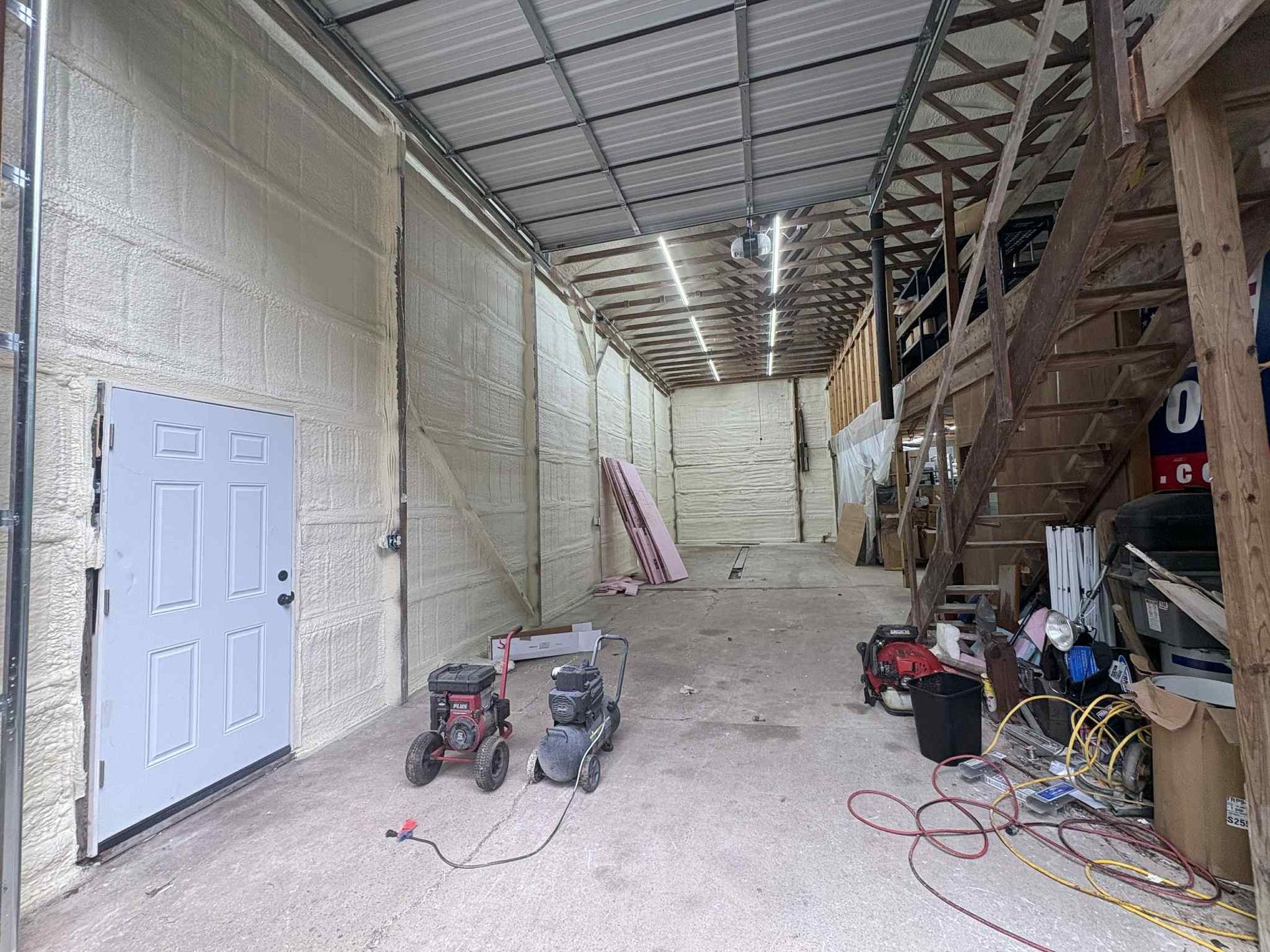 Interior view of a warehouse with a white door, machinery, and spray foam insulation.