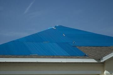 A blue tarp is covering the roof of a house.