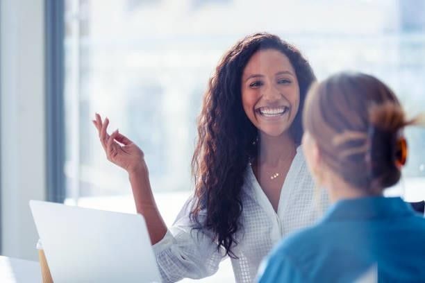 Two women are sitting at a table with a laptop and smiling.