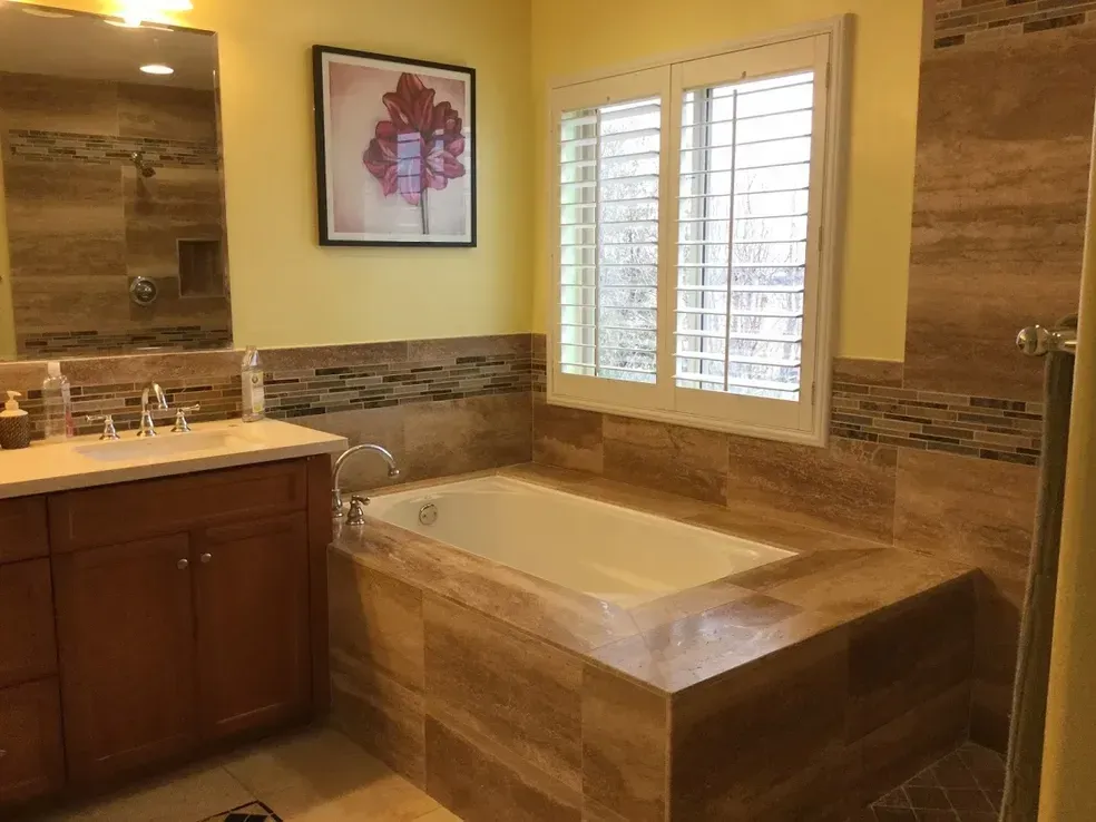 A bathroom with a tub , sink , mirror and window.