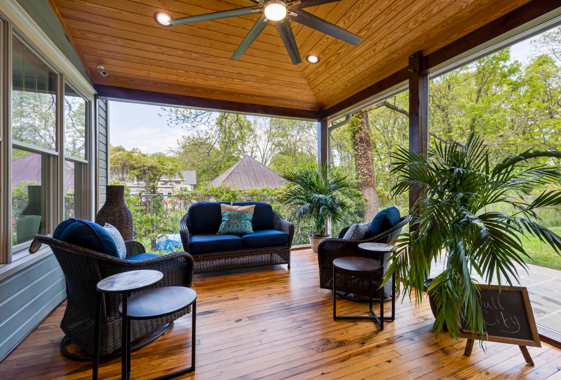 A screened in porch with a couch , chairs , tables and a ceiling fan.