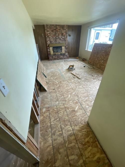 Room undergoing renovation with exposed subfloor, fireplace, and window.