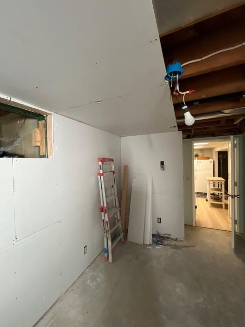 Basement under construction with drywall installed on walls and ceiling. Ladder and materials present.
