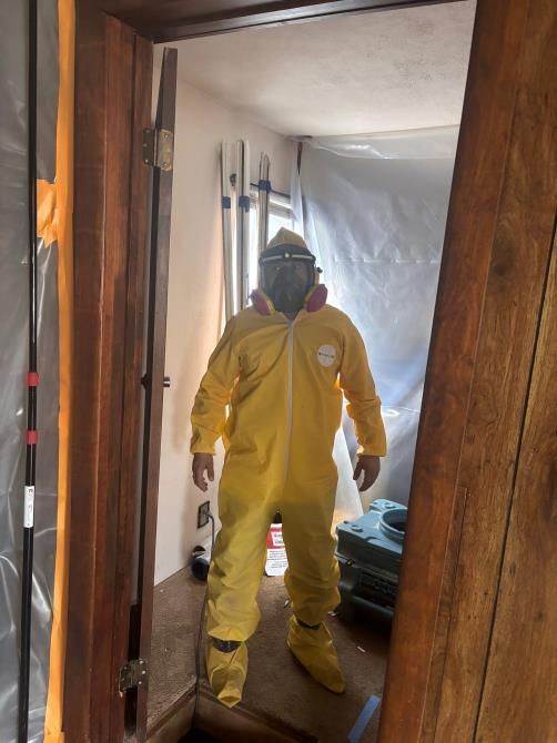 Person in yellow hazmat suit stands in a doorway, likely preparing for containment or cleanup.