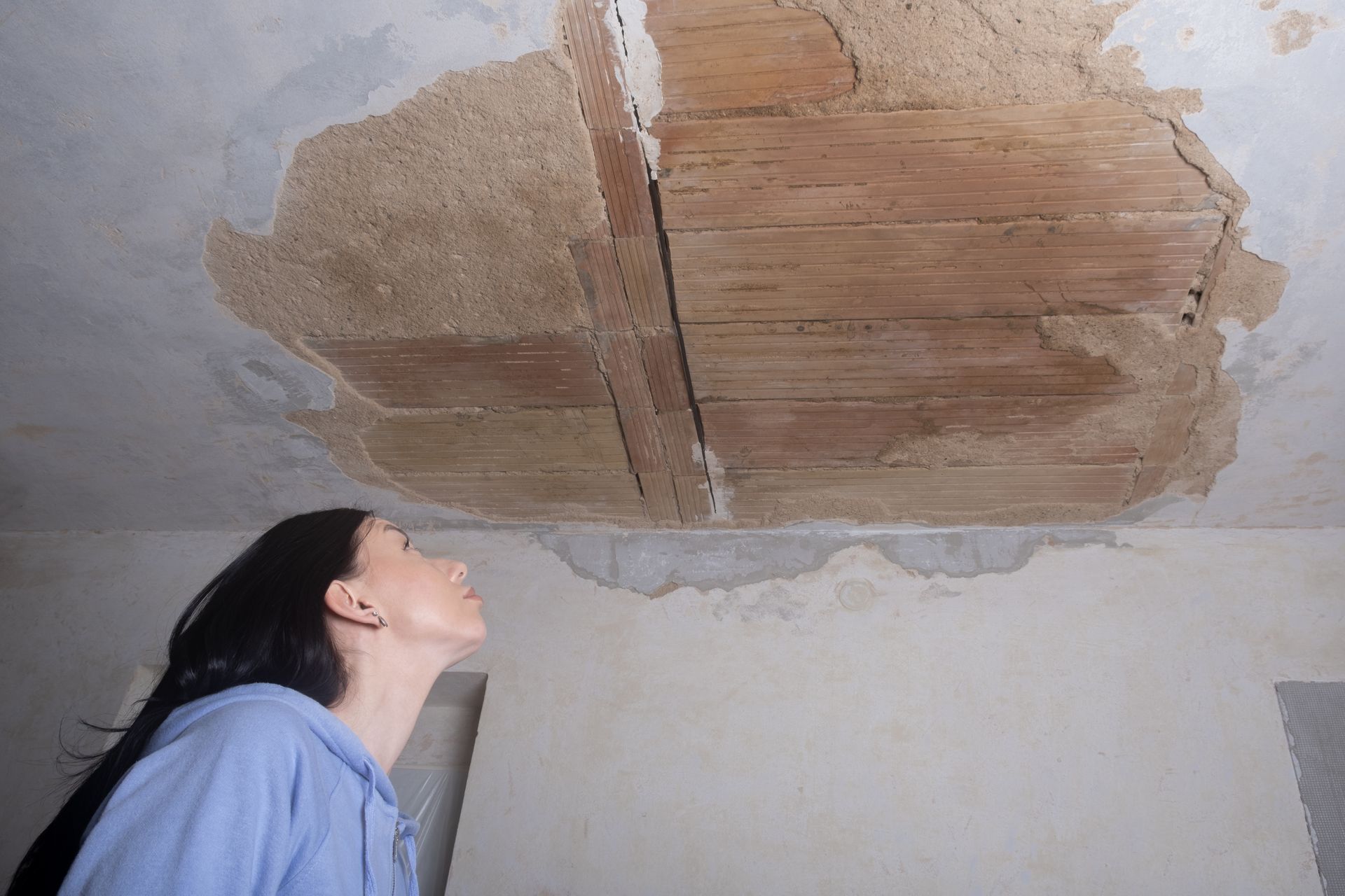 Woman looking up at a damaged ceiling with exposed wood.