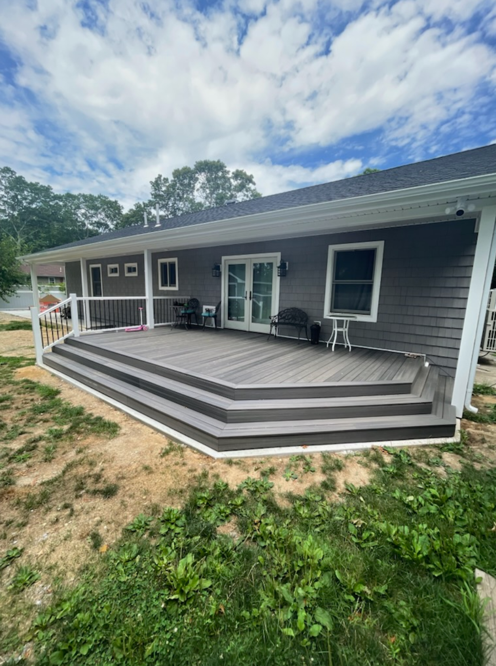 Composite deck with multiple steps on a house. Gray siding, white railings, and a blue sky.