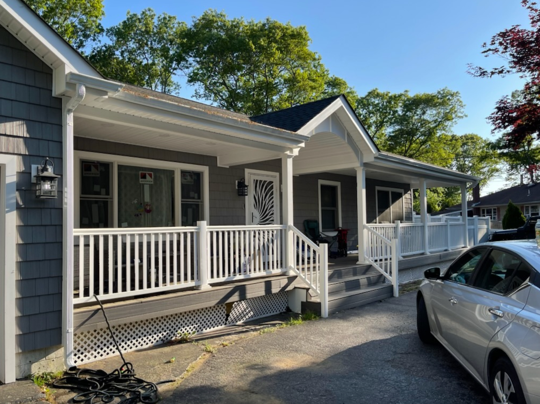 Gray house with white porch and railing; silver car parked in front.