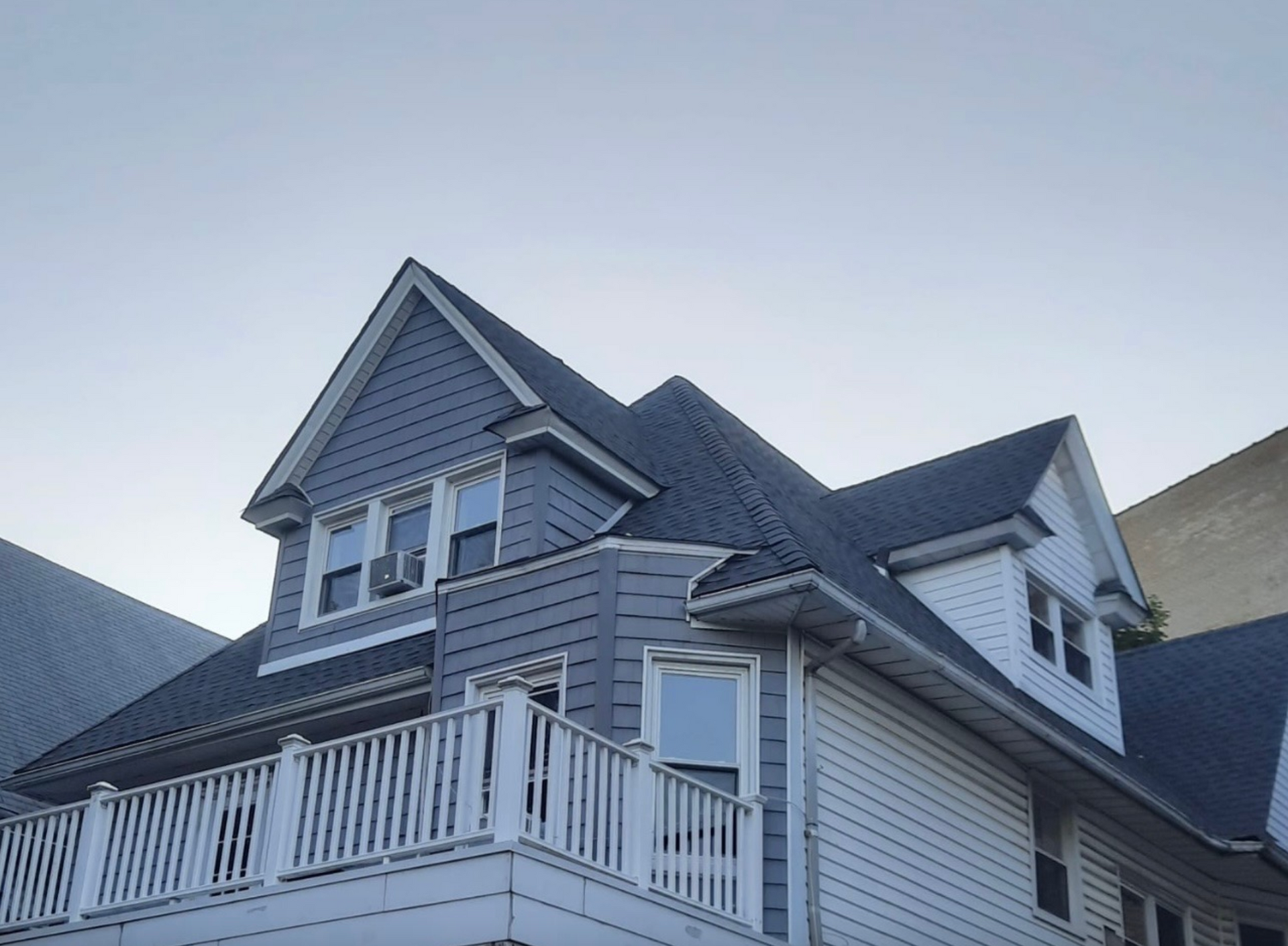 Two-story house with gray roof and siding, white balcony. Blue sky background.