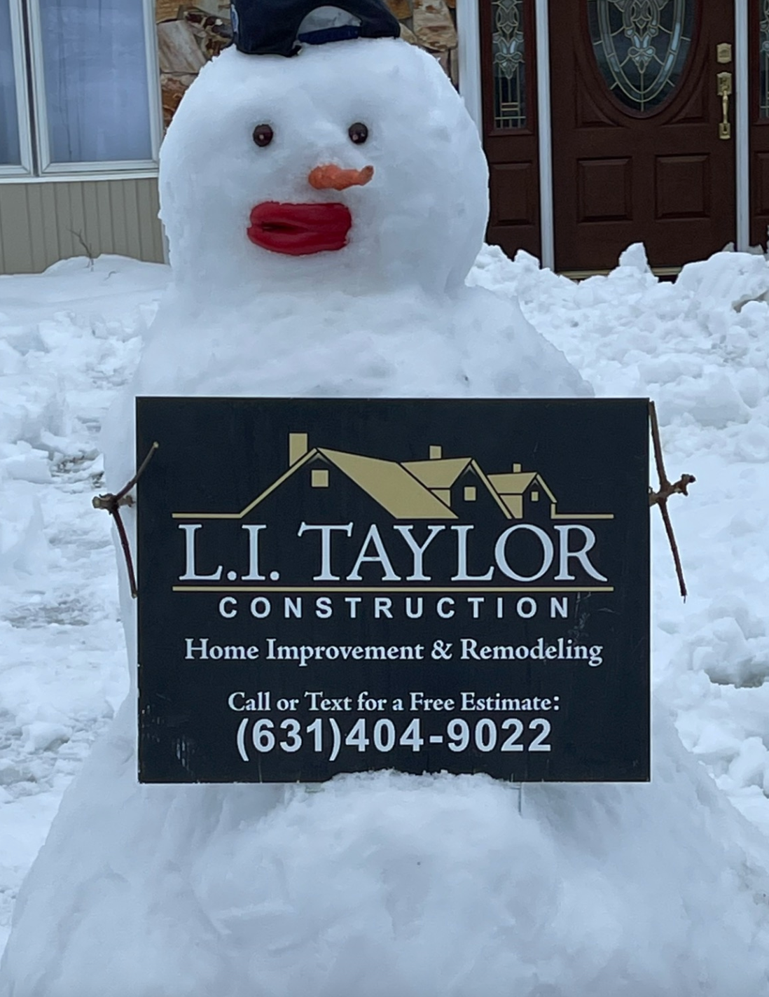 Snowman holding a sign for L.I. Taylor Construction. The snowman has a hat, red lips, and a carrot nose.
