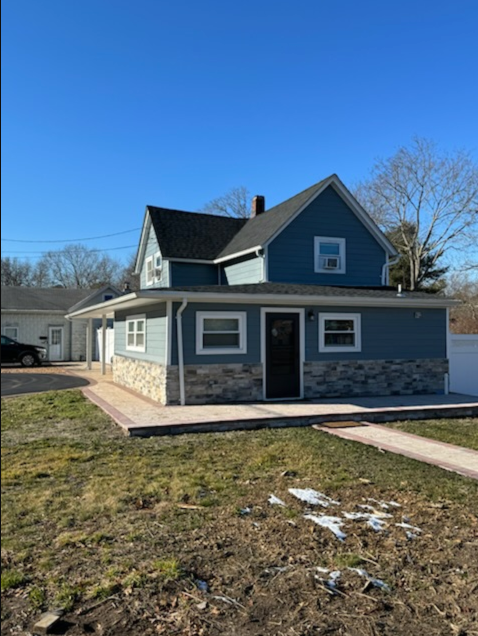 Blue two-story house with stone facade, porch, and attached garage on a sunny day.