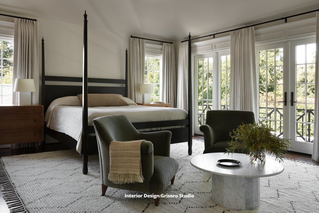 A luxury bedroom with a canopy bed , chairs , a coffee table and a large window.