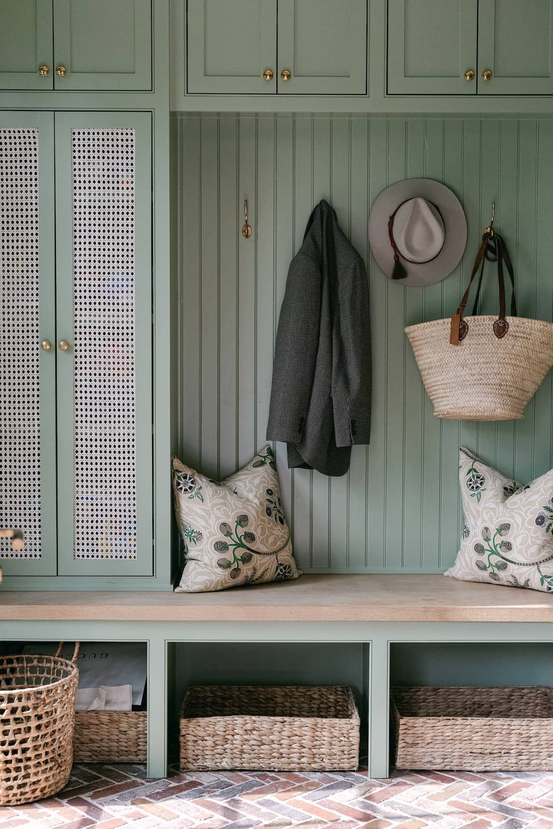 A Fort Worth mudroom with green cabinets , a bench , baskets and a hat hanging on the wall.
