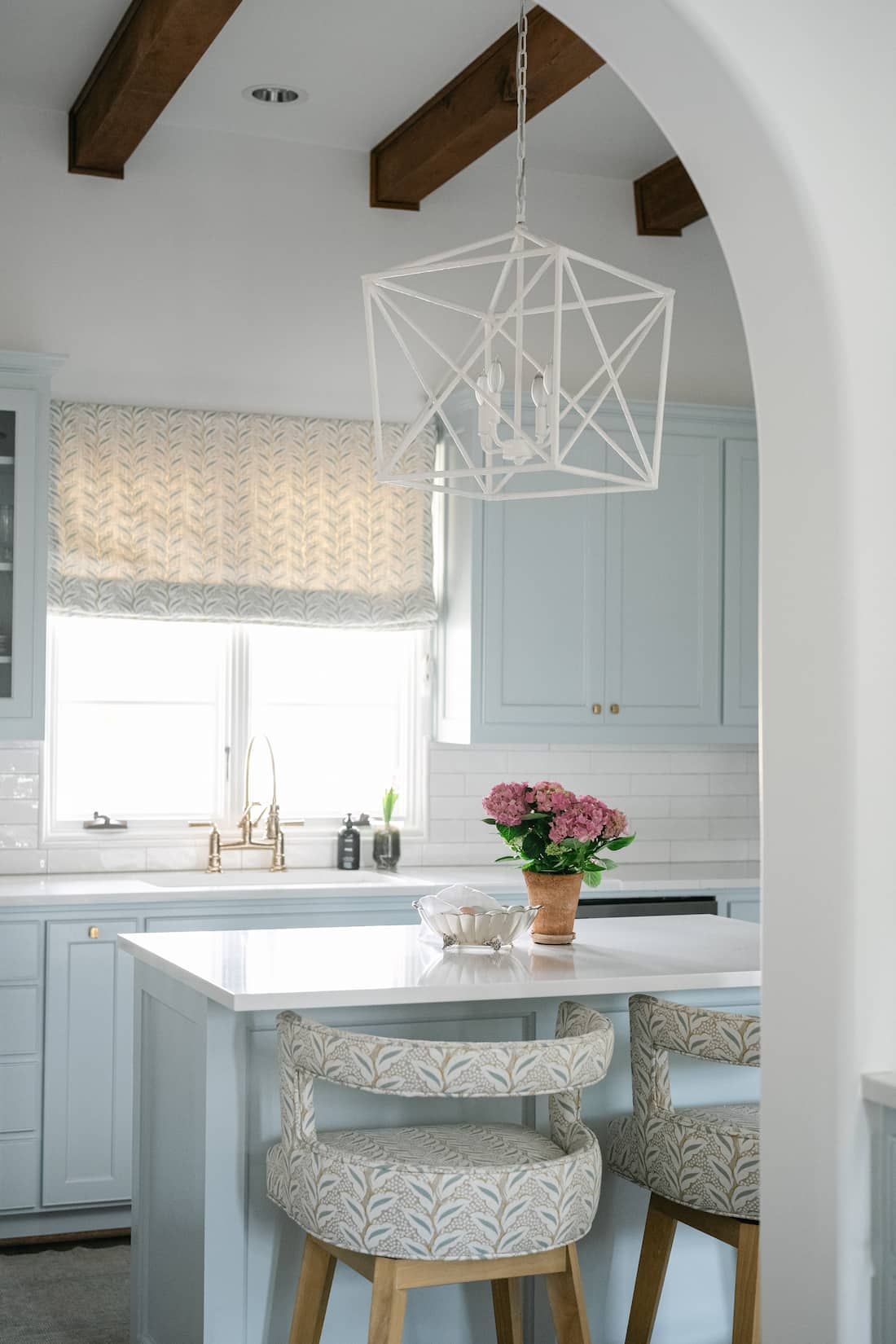 A Fort Worth kitchen with white cabinets , stools , a sink , and a pendant light.