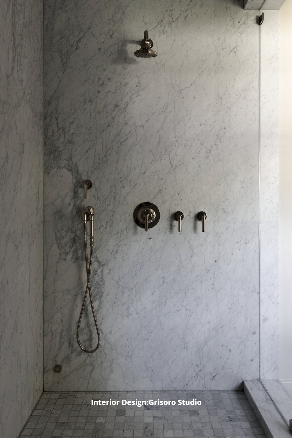 A remodeled shower with a marble wall and tile floor.