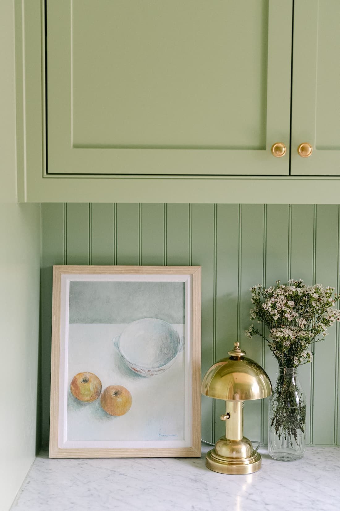 There is a painting of apples and a vase of flowers on the counter.