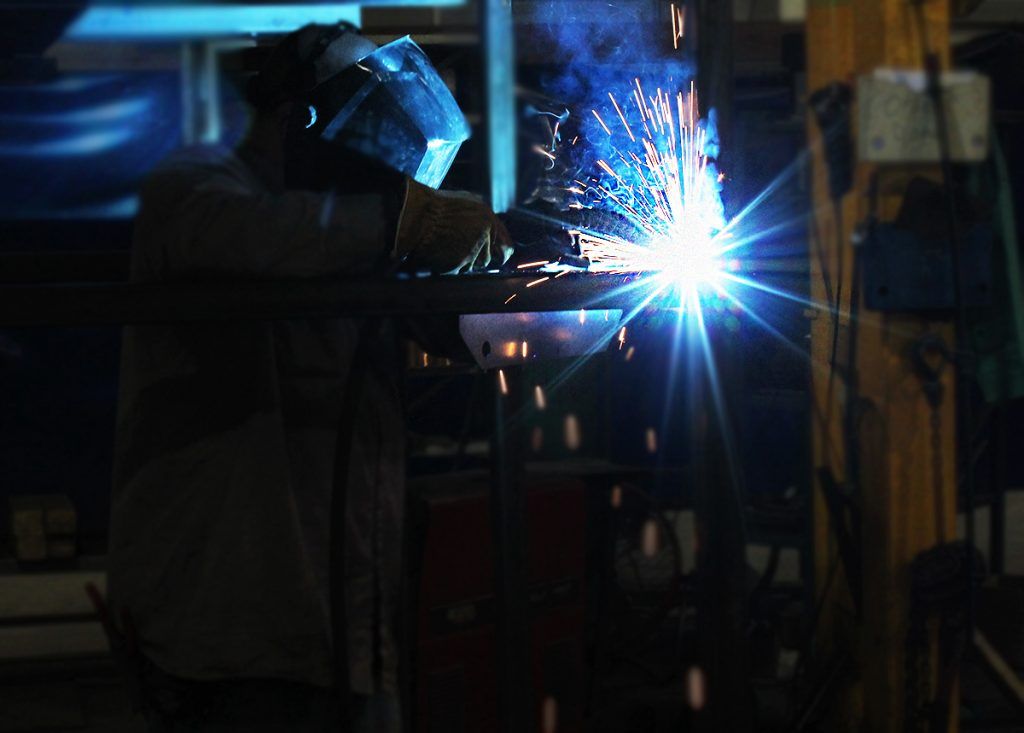 A man is welding a piece of metal in a dark room.
