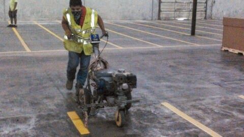 A man is painting a yellow line on the ground in a parking lot.