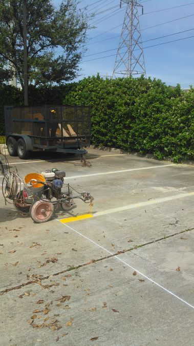 A machine is painting a yellow line on a parking lot.