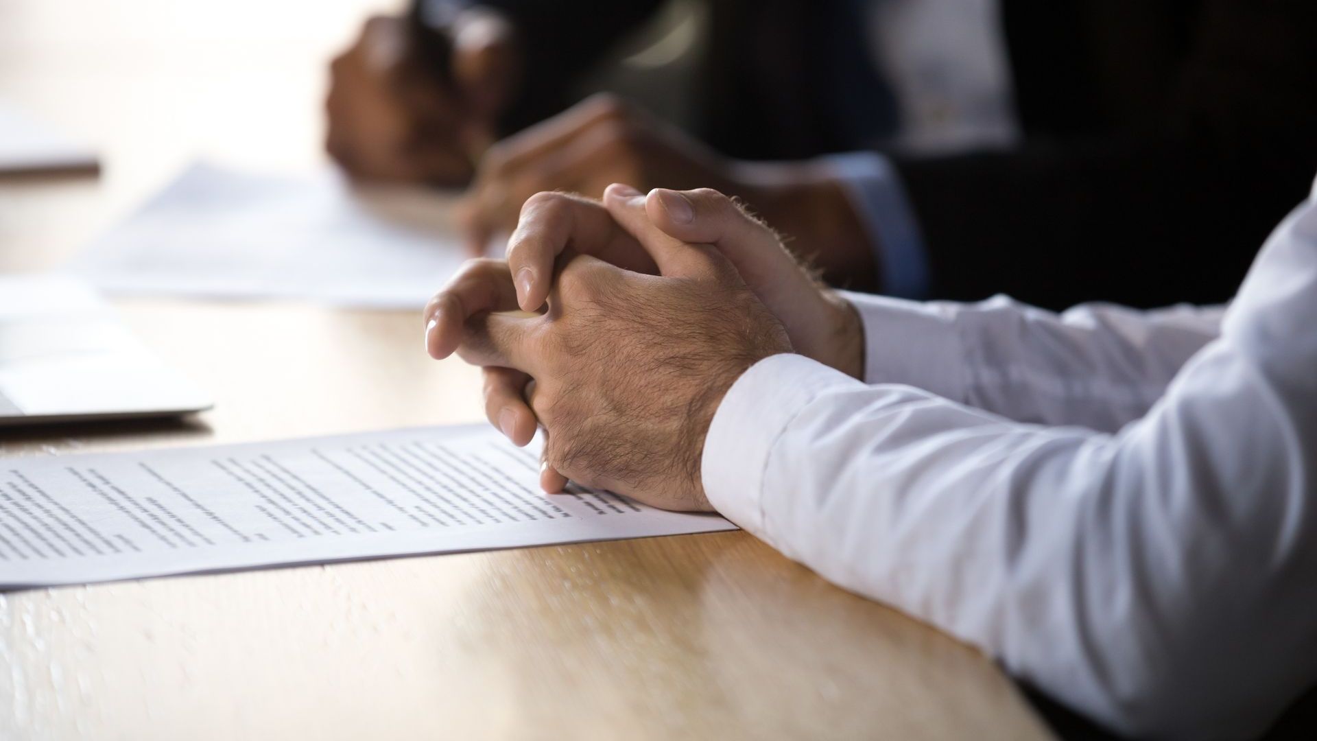 A man is sitting at a table with his hands folded over a piece of paper.