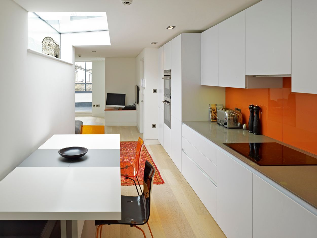 Modern white kitchen with orange backsplash, dining table, and chair near a bright window