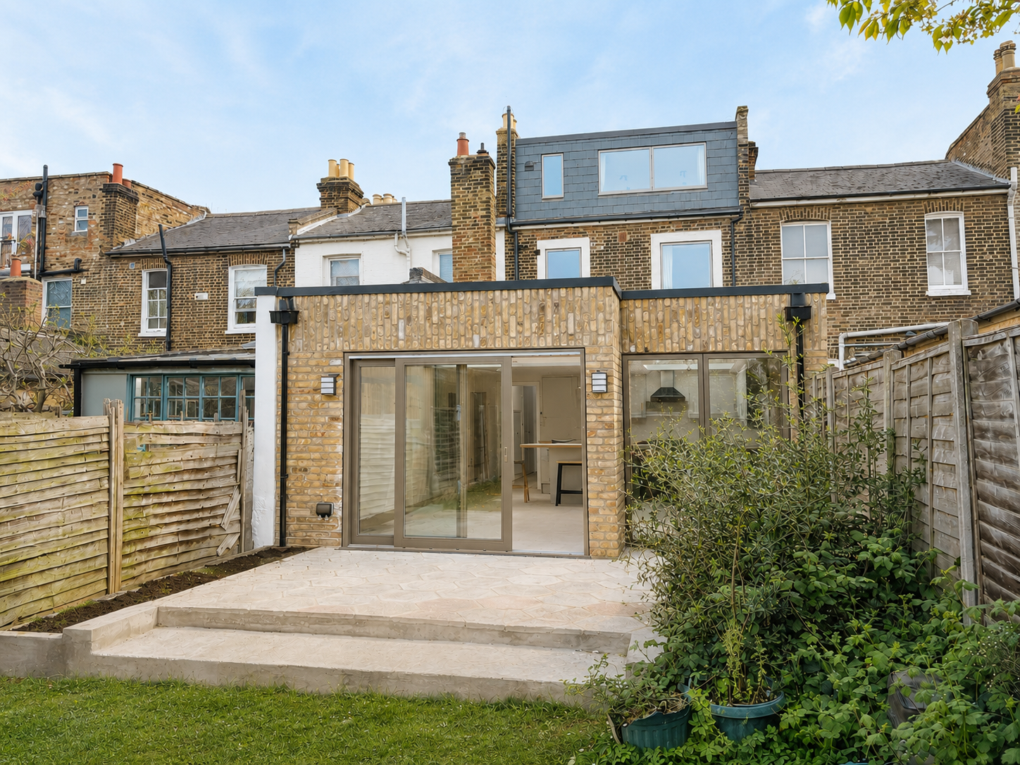Modern glass extension with patio in front of a stone house and garden beyond