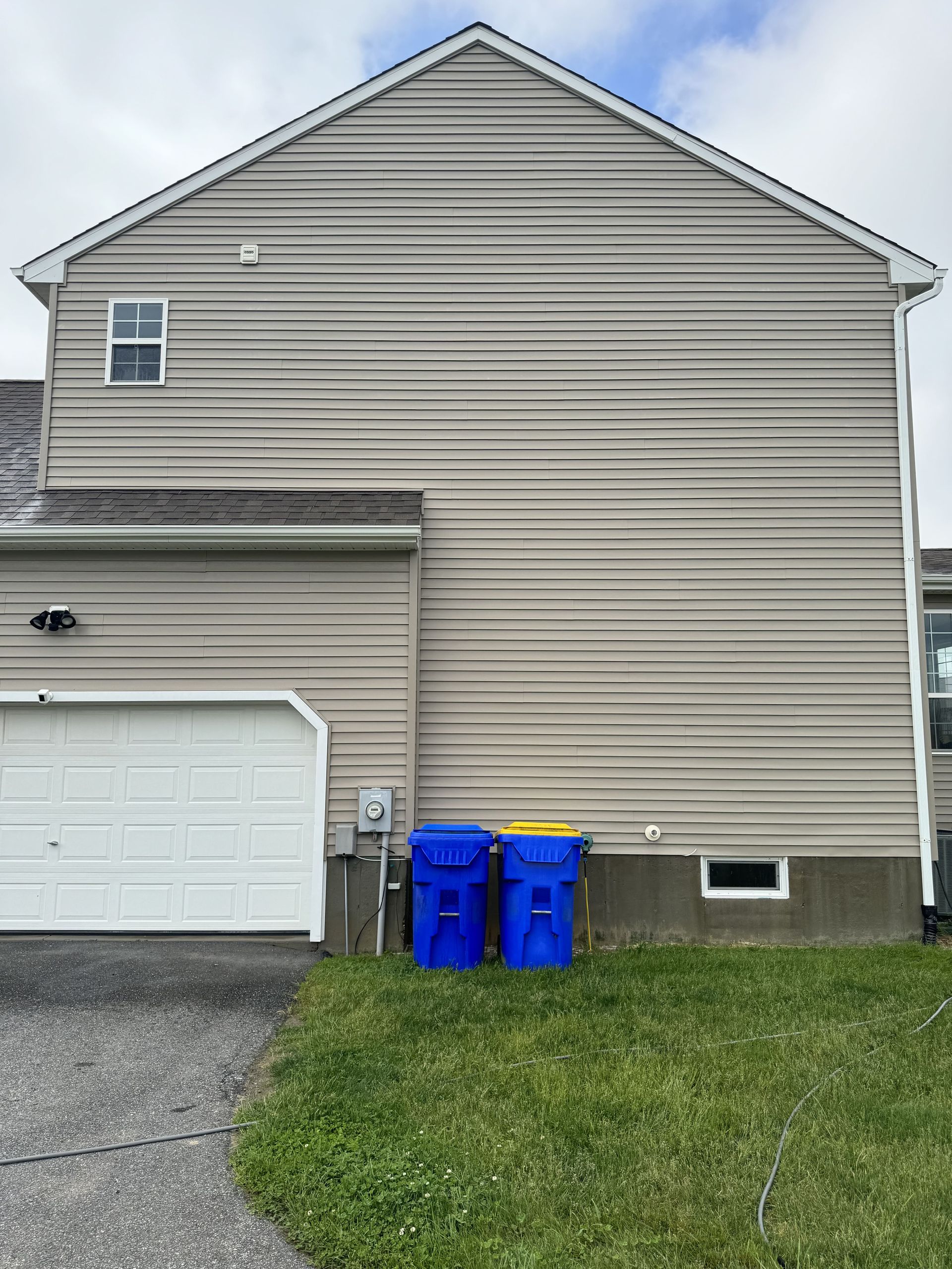 Side view of a beige house with a white garage door, two blue trash bins on the grass.