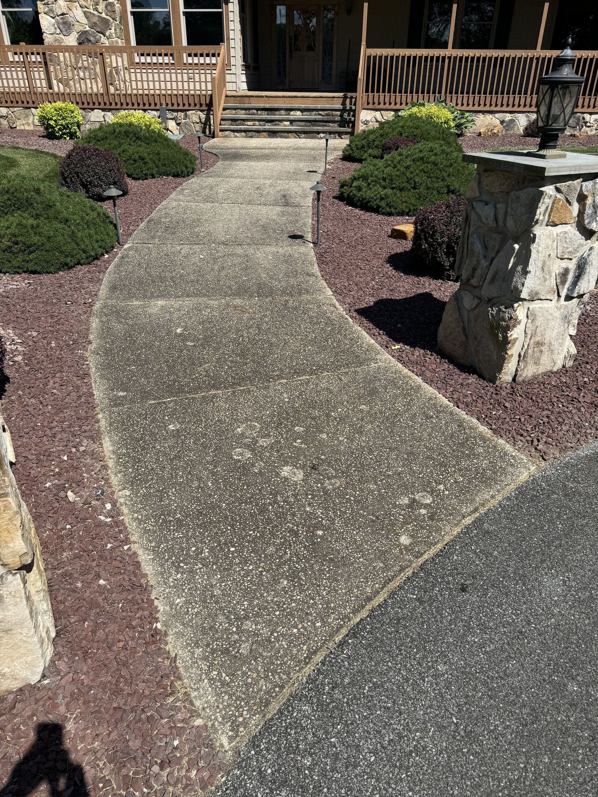Curving concrete walkway to a house entrance, bordered by red gravel and landscaping.