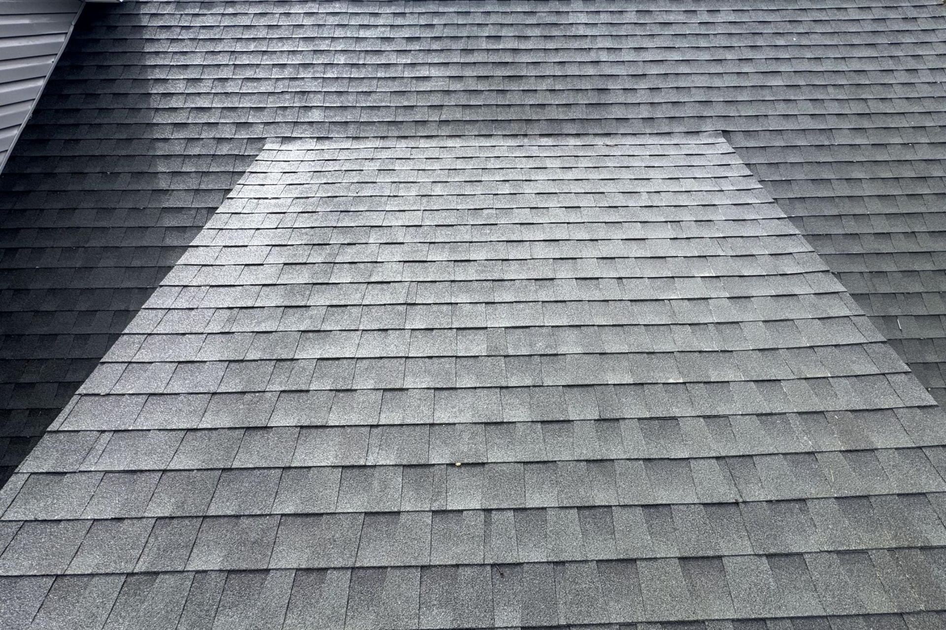 Gray asphalt shingle roof with a square patch of newer, lighter shingles.