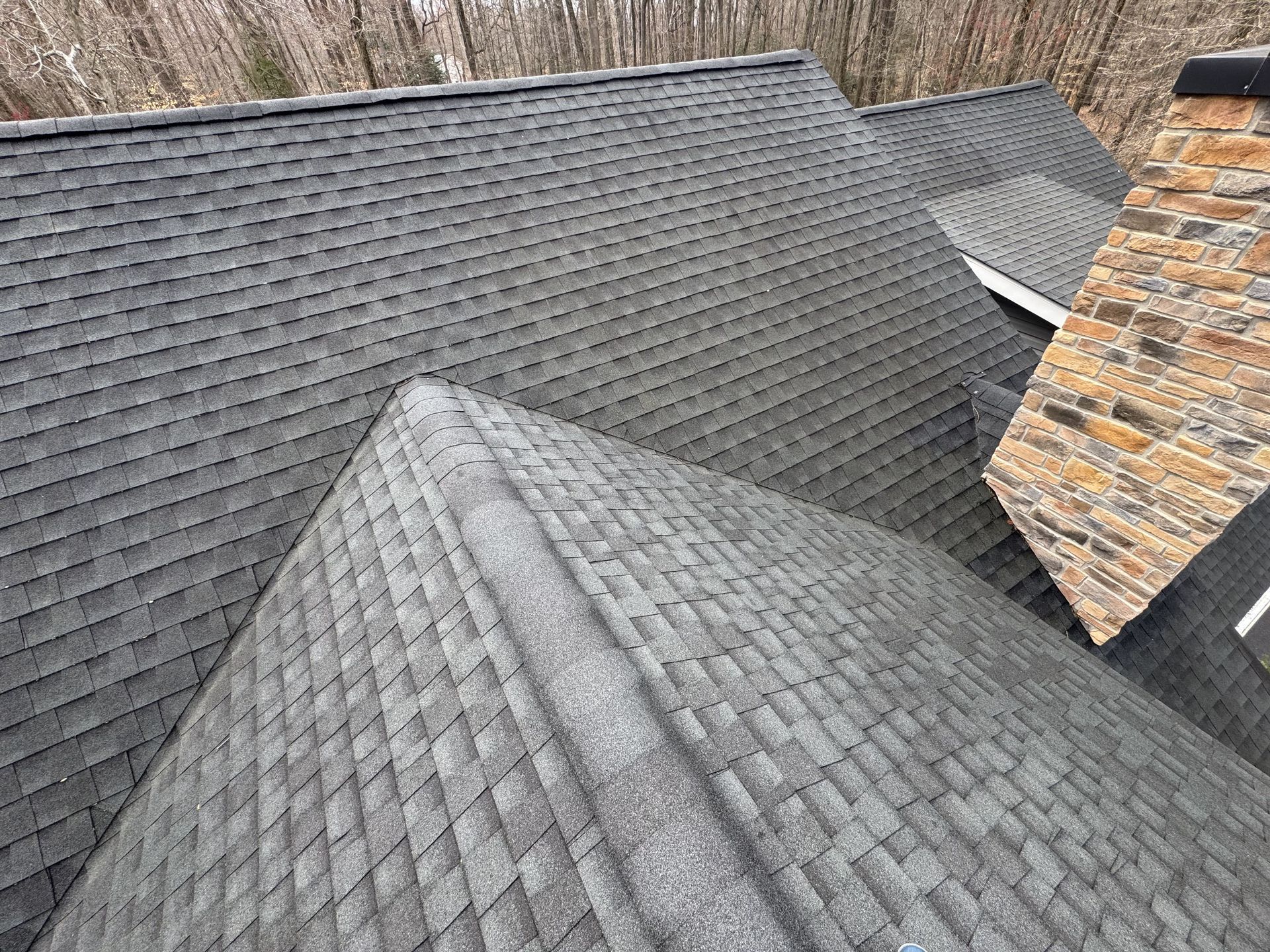 Gray asphalt shingle roof with a chimney and trees in the background.