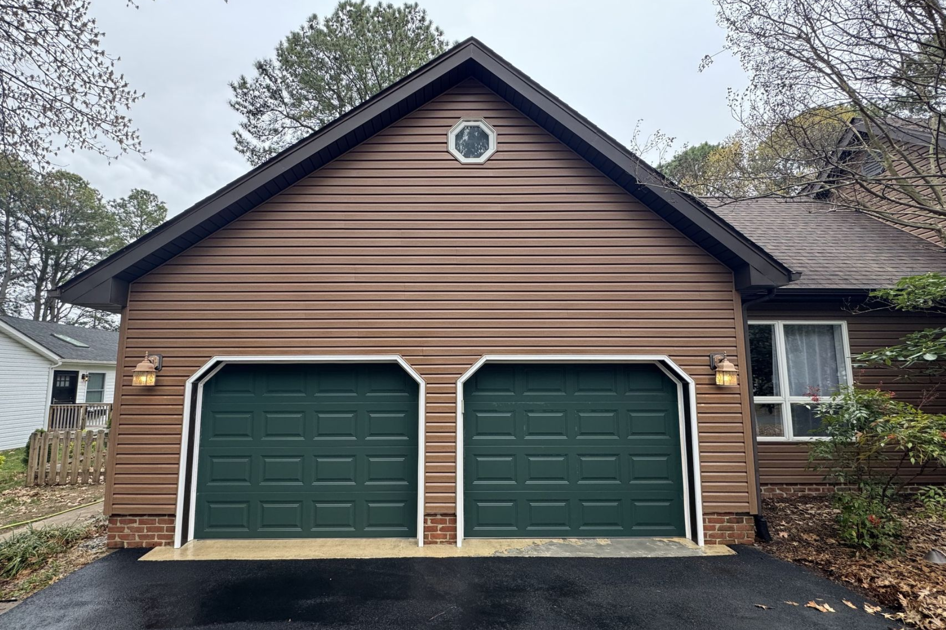 Brown garage with two green doors, a round window, and a black roof.