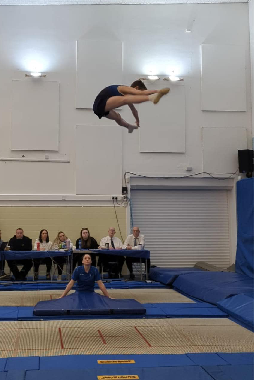 A woman is doing a trick on a trampoline while people watch.