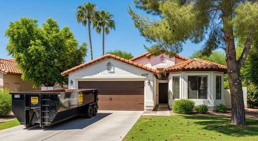 House with dumpster in driveway, brown garage door, clay tile roof, green lawn, sunny day.